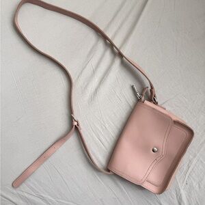 A small pink crossbody bag with adjustable strap.